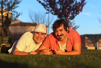 Portrait of couple of gay men lying on the grass looking at camera, normal people. LGBT love concept