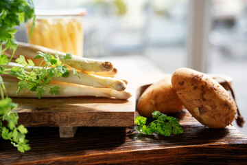 Seasonal white asparagus with raw potatoes and fresh parsley on rustic wooden board. Healthy eating concept background with space for text.