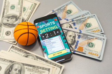 Smartphone with gambling mobile application and basketball ball with money close-up. Sport and betting concept