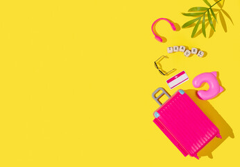 Flat lay pink toy suitcase with travel accessories on a yellow background. Travel concept.