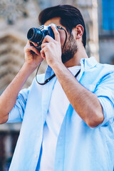 Male photographer focusing and making photos on modern camera enjoying beauty of old architectural city during summer vacation.Casual dressed tourist taking pictures spending free time on hobby