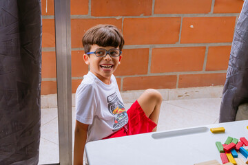 International Children Day. Beautiful latin boy playing with colored blocks on a white table. Playful, creative and thinking games. Family day, happy children. - obrazy, fototapety, plakaty
