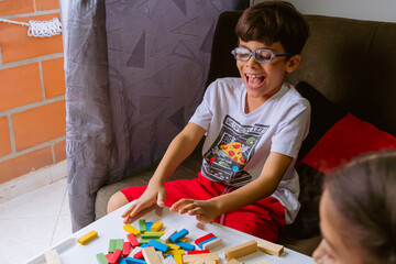 International Children Day. Beautiful latin boy playing with colored blocks on a white table. Playful, creative and thinking games. Family day, happy children. - obrazy, fototapety, plakaty