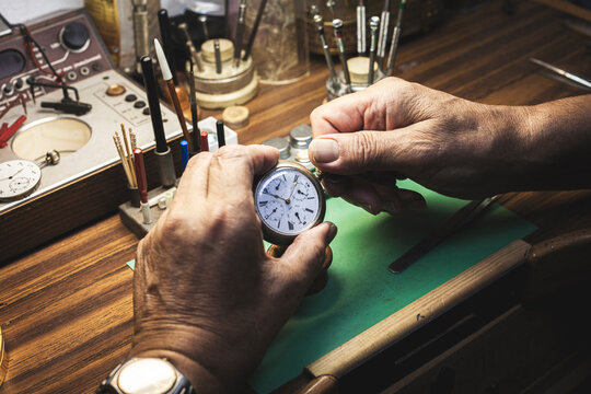 The expert hands of a watchmaker turn the crown of a watch with precision.