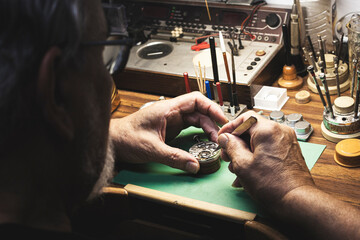 Watchmaker at his workbench full of tools where he repairs a clock machine.