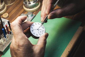 Watchmaker's hands using tweezers to place the hour hand of a watch.