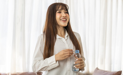 Portrait asian beauty body slim woman drinking water from a bottle while relax and feeling fresh,  refresh drink, wellness, diet, healthcare, mineral at home.Healthy liquid lifestyle concept