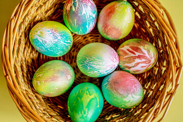 Easter colored bright decorated pastel eggs of blue, blue, green, pink, yellow, and lie in a wicker basket on a yellow background