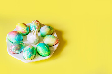 Easter colored bright decorated pastel eggs of blue, blue, green, pink, yellow, and lie on a porcelain white plate with an Easter bunny rabbit on a yellow background