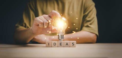 New idea concept with innovation and inspiration, hand touching on light bulb on wood block with...