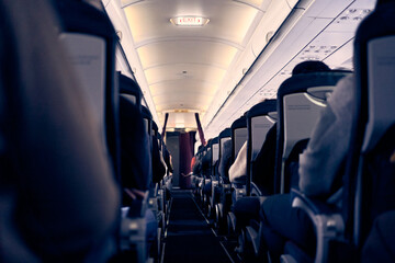 Unrecognizable people in the cabin of a commercial aircraft with rows of seats along the aisle....