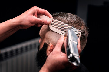 A man gets a haircut at the barber shop. The barber uses a white comb and an electric razor.