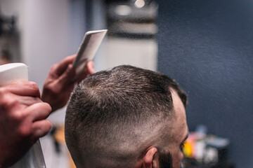 A man is getting his hair cut by a barber. The barber is using a comb and a spray bottle to style...