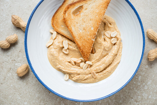 Blue and white plate with peanut butter and toasts, horizontal shot on a beige stone background, above view, middle close-up
