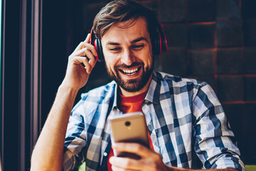 Cheerful bearded hipster guy choosing song in music app to listen in modern headphones connected...
