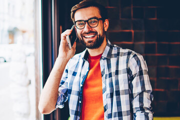 Portrait of happy bearded young man dressed in trendy shirt smiling at camera while talking with...