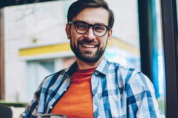 Half length portrait of successful bearded young man in eyeglasses for vision correction smiling at...