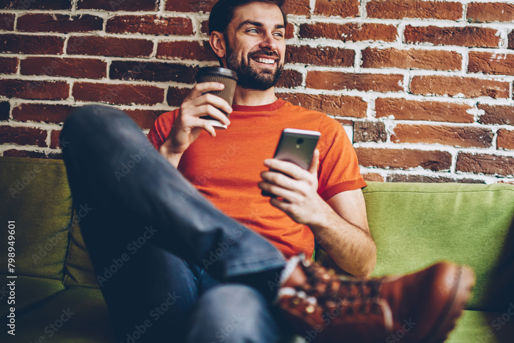 Poster positive bearded bogger with coffee to go in hand smiling and looking away while installing mobile a