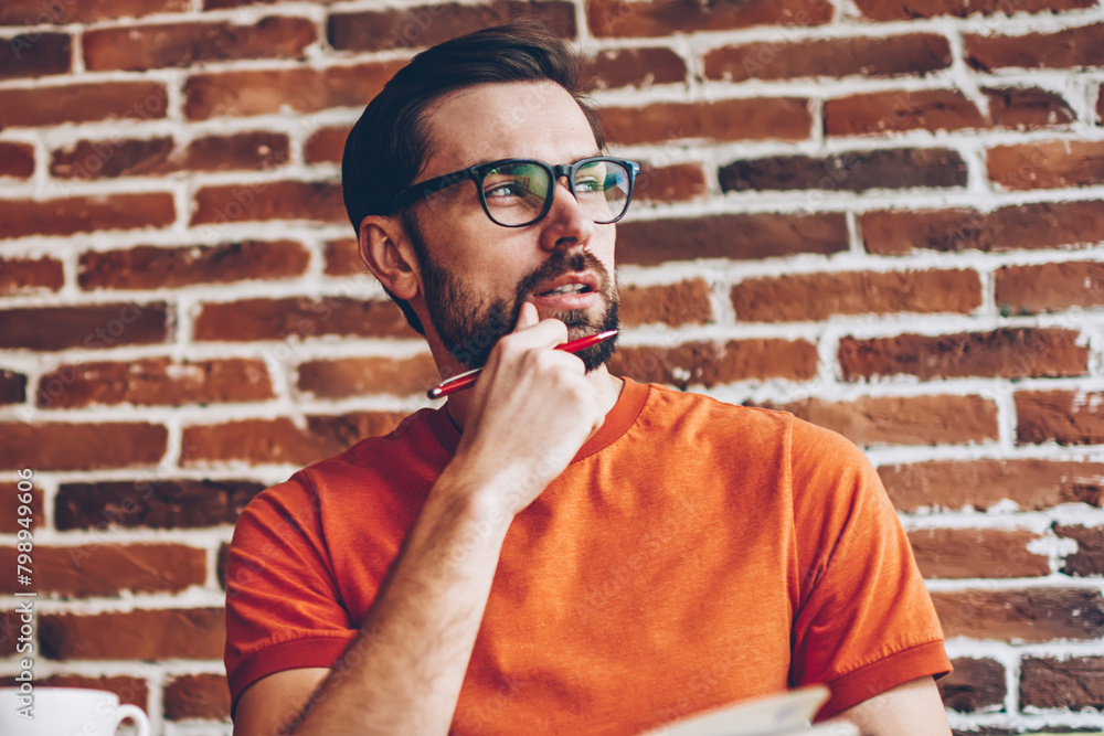 Poster thoughtful bearded male blogger with notepad in hands looking on side and thinking on creative idea 