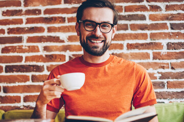 Portrait of bearded young man in eyeglasses for vision correction laughing at camera while enjoying...