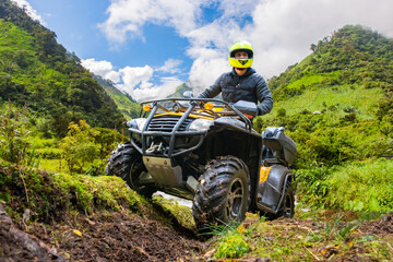 Man on quad bike. Motorcyclist in green mountains. Man ATV driver in yellow helmet. All-terrain motorcycle for off-road driving. Guy drives ATV. ATV driver looks ahead. Quad bike race © Grispb