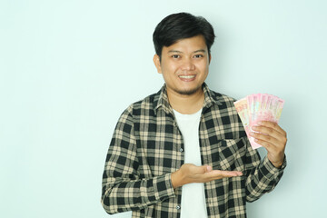 Young Asian man wearing brown flannel shirt smiling happy while holding money with his open right...