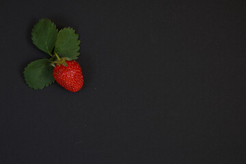 A red strawberry with leaves on a black background.