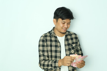 Young Asian man wearing brown flannel shirt smiling happy when counting money that he hold