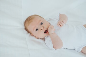 newborn baby boy smiling on a white bed at home, family with a small child, close-up, place for text