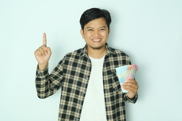 Young Asian man holding paper money while pointing his right finger up and smiling
