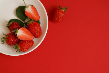 Red strawberries on white plate on red background top view.