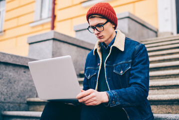 Pensive hipster student reading mail and notification on laptop computer connected to free 4G...