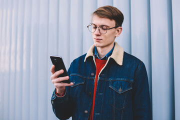 Young hipster blogger checking mail and messaging with followers in social network on smartphone...