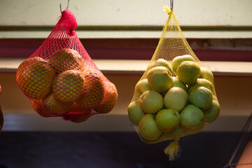 Net bags holding a supply of fresh oranges and apples at a juice stand.