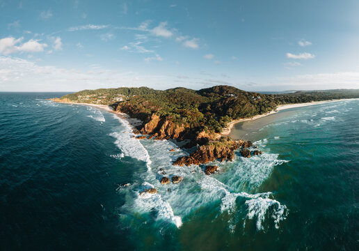 Byron Bay lighthouse and the pass high on the rocky headland - the most eastern point of Australian continent facing Pacific ocean in elevated aerial seascape above coast.