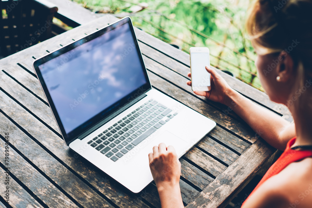 Aufkleber back view of millenial woman holding mobile phone while synchronizing multimedia files with netbook,