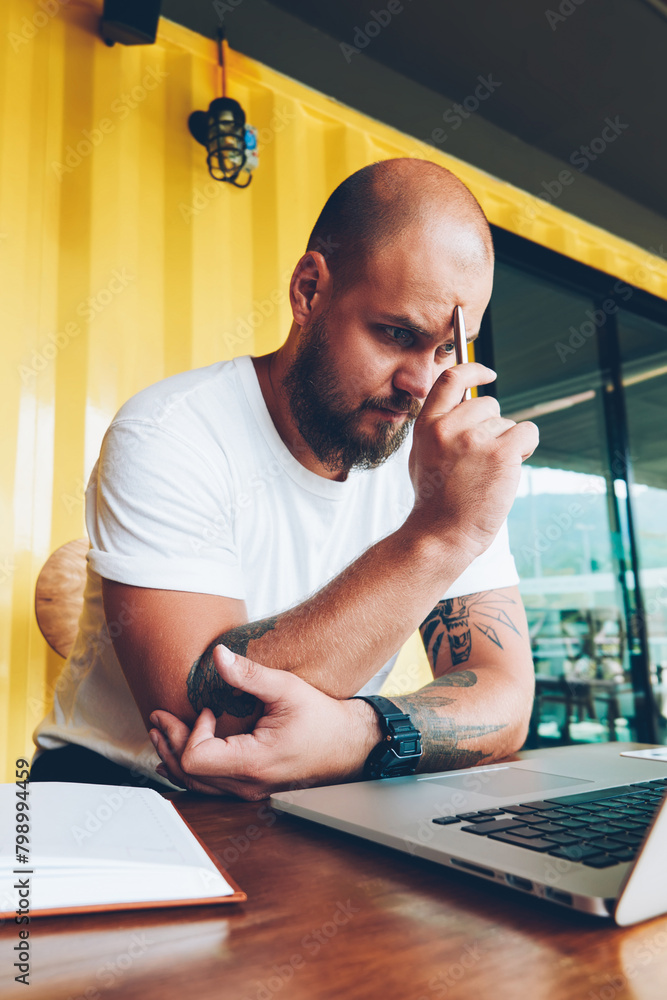 Poster concentrated male student puzzled on solving problem watching online tutorial during courses via lap