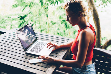 Skilled female freelancer working online via laptop computer sitting on terrace in cafe looking at...