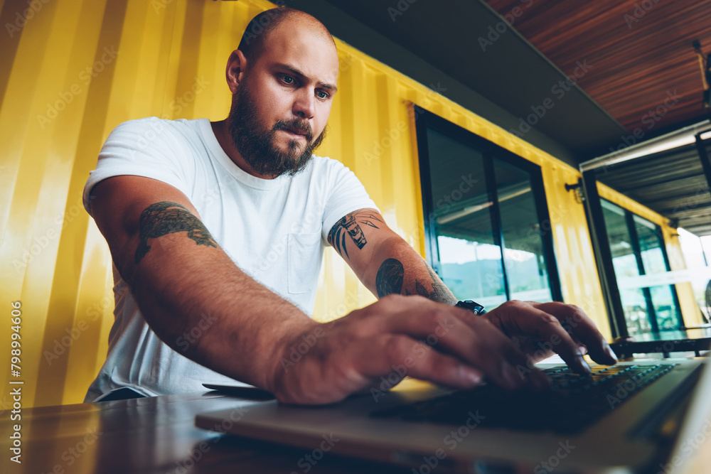 Poster worried caucasian hipster guy concentrated on playing video game on laptop computer, serious millenn