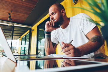 Contemplative bearded hipster guy concentrated on idea for publication working on freelance using...
