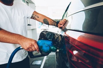 Cropped image of male holding nozzle charging vehicle car with petrol and oil on station, young man pumping benzene to automobile tank through hose on service, environment pollution concept - Powered by Adobe