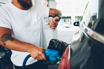 Cropped image of hipster guy looking at wristwatch while pumping his car with petrol benzene on...