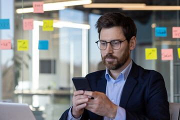 A man in a suit is looking at his cell phone. Concept of modernity and technology, as the man is using his phone in a professional setting. The man's facial expression