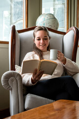 Mujer leyendo un libro sentada cómodamente en el sofá de su sala de estar. Fotografia vertica