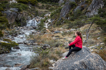 Mujer turista senatada en una roca mientras disfruta de las vistas de un bosque patagonico y sus arroyos