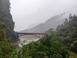 Taroko, Taiwan - 11.26.2022: Red metal Shakadong Bridge over Liwu River connecting tunnels in a mist with staircase to Shakadong Trail in maintenance and mountains at the back before 403 earthquake