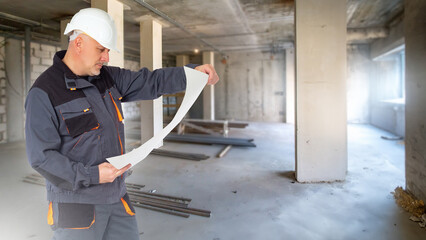 Man builder. Guy is engineer. Architect in building under construction. Builder studies work plan. Architect in gray uniform. Man repairman in unfinished building. Construction bureau contractor