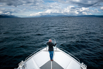 Mujer parada en la proa de un barco mientras disfruta de su excursión de navegación por el canal de Beagle - obrazy, fototapety, plakaty