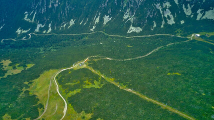 High mountain trails winding through lush green forests and clouds, offering breathtaking landscapes captured by drone aerial photography. Experience the essence of the mountains and nature.