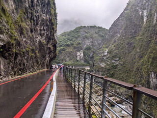 Taroko, Taiwan - 11.26.2022: Tourists with helmets walking on Swallow Grotto Trail with a car along Liwu River and marble cliffs with concrete pillars in sight during pandemic before 403 earthquake